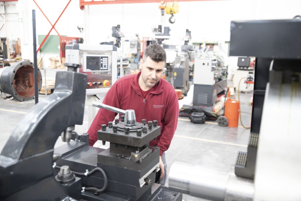 Operario realizando mecanizado de piezas de precisión en un torno industrial en taller metalúrgico.
