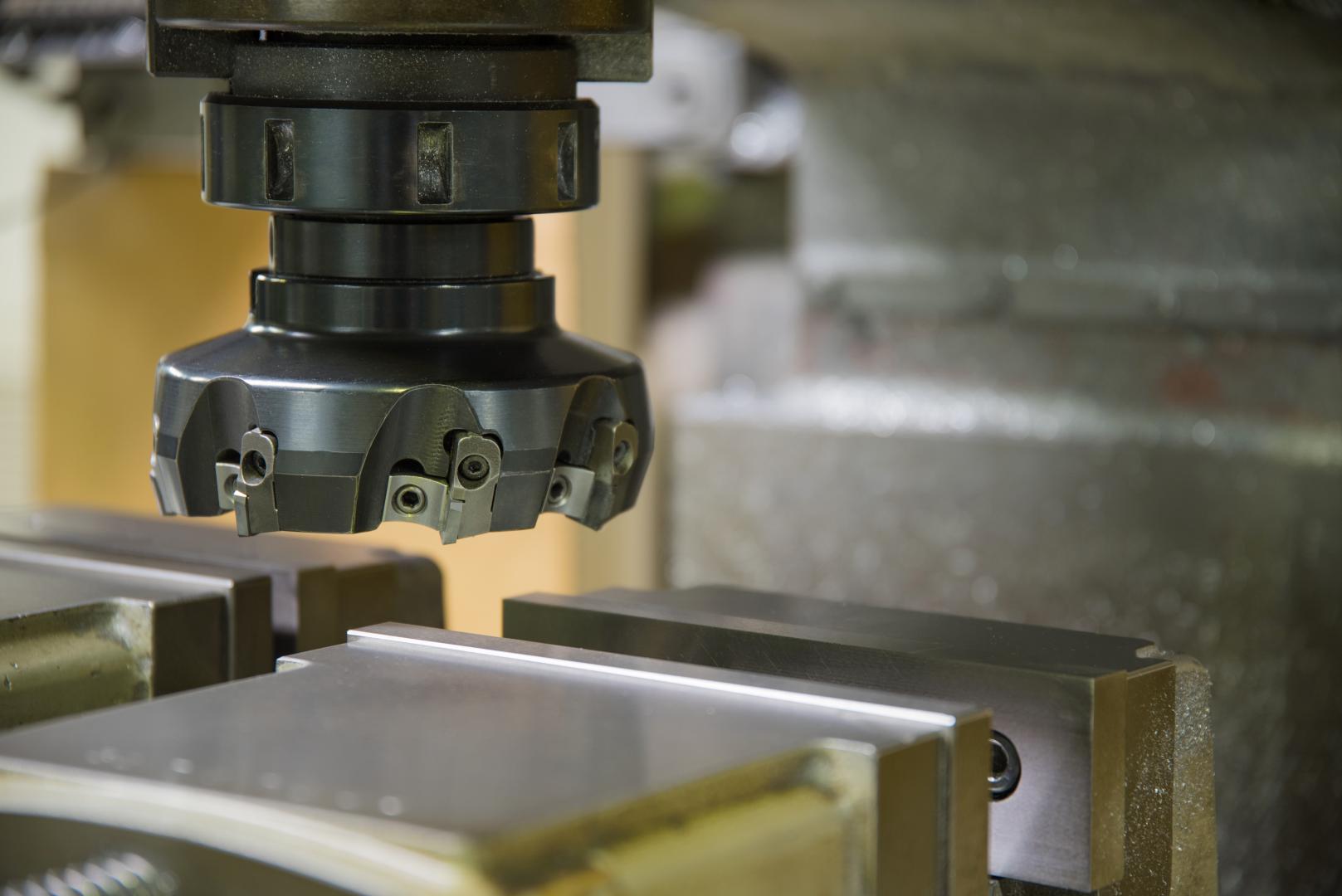 Cabezal de fresadora industrial con fresa de planear sobre una pieza de metal sujeta en un tornillo de banco.