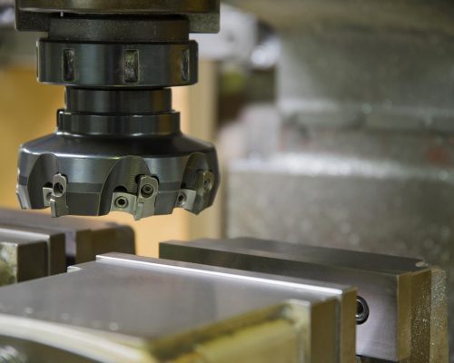 Cabezal de fresadora industrial con fresa de planear sobre una pieza de metal sujeta en un tornillo de banco.
